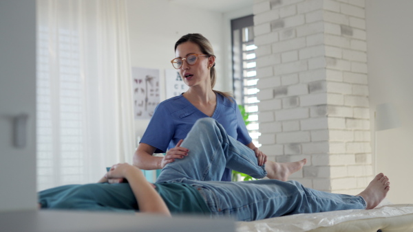 Physiotherapist doing manual therapy, exercise with teenage boy's knee, rehabilitation. Orthopedist examining and treating painful injured knee of young athlete. Concept of teen preventive health care.