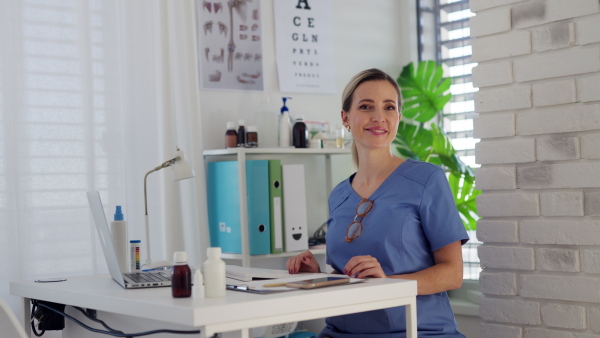 Video of a beautiful female doctor with eyeglasses, sitting at the desk in a doctor's office.