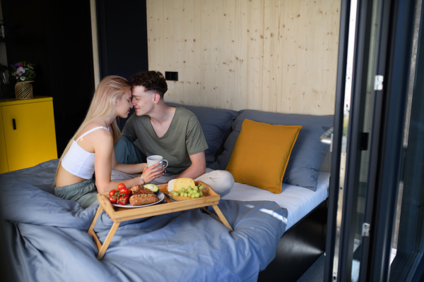 A young beautiful couple in love is sitting in bed and having healthy breakfast together.