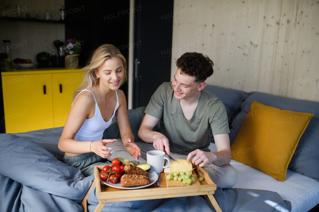 A young beautiful couple in love is sitting in bed and having healthy breakfast together.