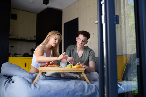 A young beautiful couple in love is sitting in bed and having healthy breakfast together.