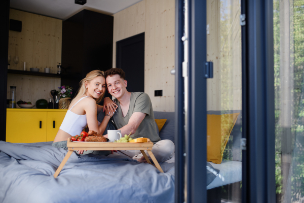 A young beautiful couple in love is sitting in bed and having healthy breakfast together.