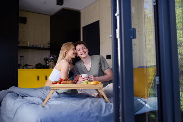 A young beautiful couple in love is sitting in bed and having healthy breakfast together.