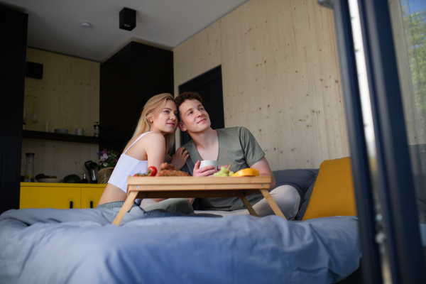 A young beautiful couple in love is sitting in bed and having healthy breakfast together.