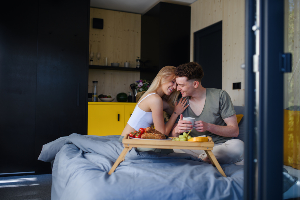 A young beautiful couple in love is sitting in bed and having healthy breakfast together.