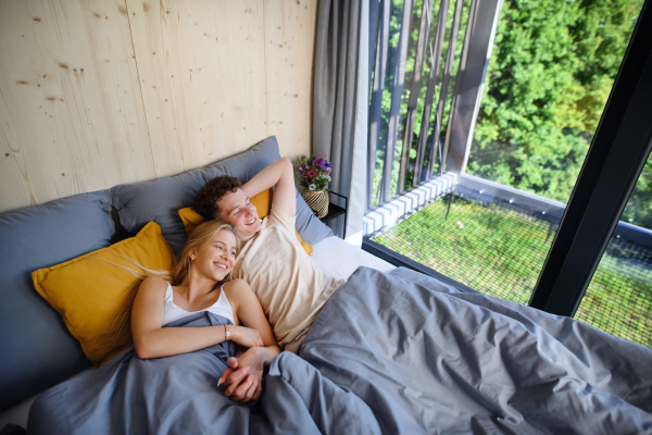 A young happy couple in love lying in bed in morning in their new home in tiny house, sustainable living concept.