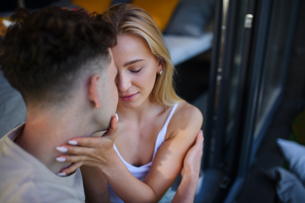 A young couple in love cuddling and kissing outdoors on terrace, weekend away in tiny house in countryside, sustainable living.