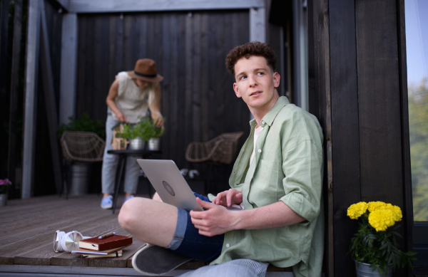 A happy young couple with laptop resting outdoors in a tiny house, weekend away and remote office concept.