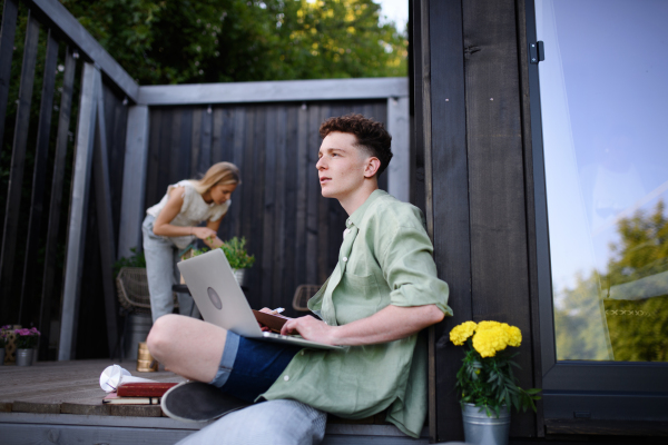 A happy young couple with laptop resting outdoors in a tiny house, weekend away and remote office concept.