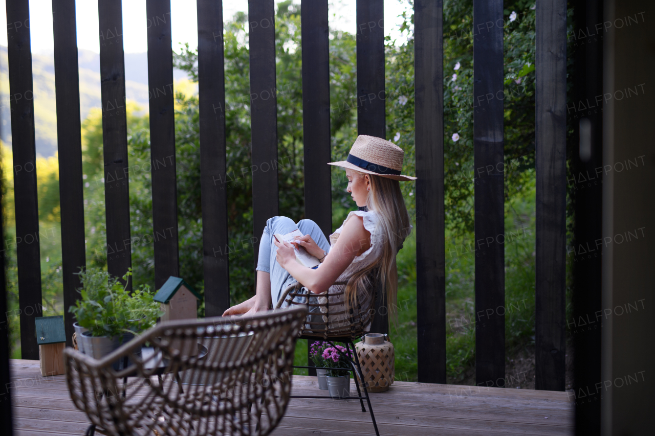 A young beautiful woman relaxing on cozy terrace, reading a book, digital detox and weekend away concept.