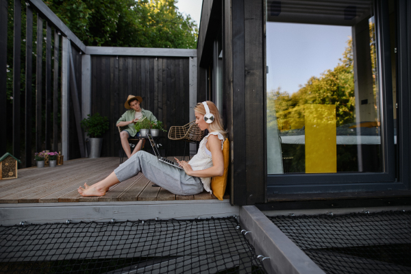 A happy young couple with laptop resting outdoors in a tiny house, weekend away and remote office concept.