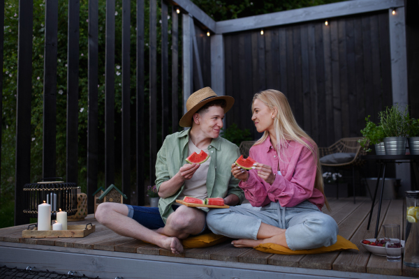 Cheerful young couple in love eating a watermelon together at terrace.