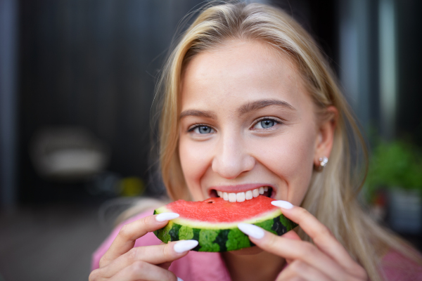 A portrait of beautiful young woman eating watermelon and looking at camera.