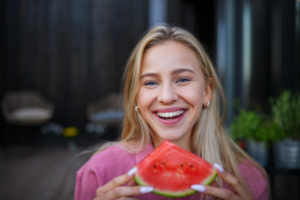 A portrait of beautiful young woman eating watermelon and looking at camera.