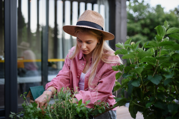 A young woman taking care of her herbs on terrace in tiny house, sustainable living.