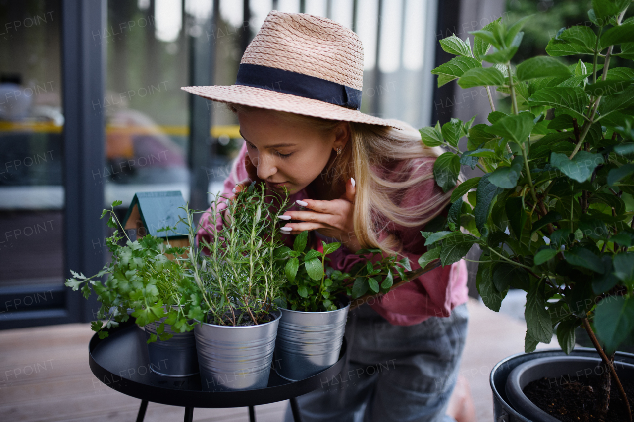 A young woman taking care of her herbs and smelling thme on terrace in tiny house, sustainable living.