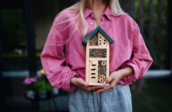 A young woman holding bug and insect hotel on terrace in garden, sustainable lifestyle. Close-up.