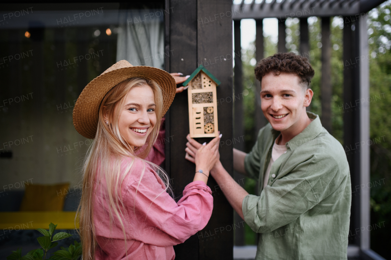 A young couple holding bug and insect hotel on terrace in garden, sustainable lifestyle.