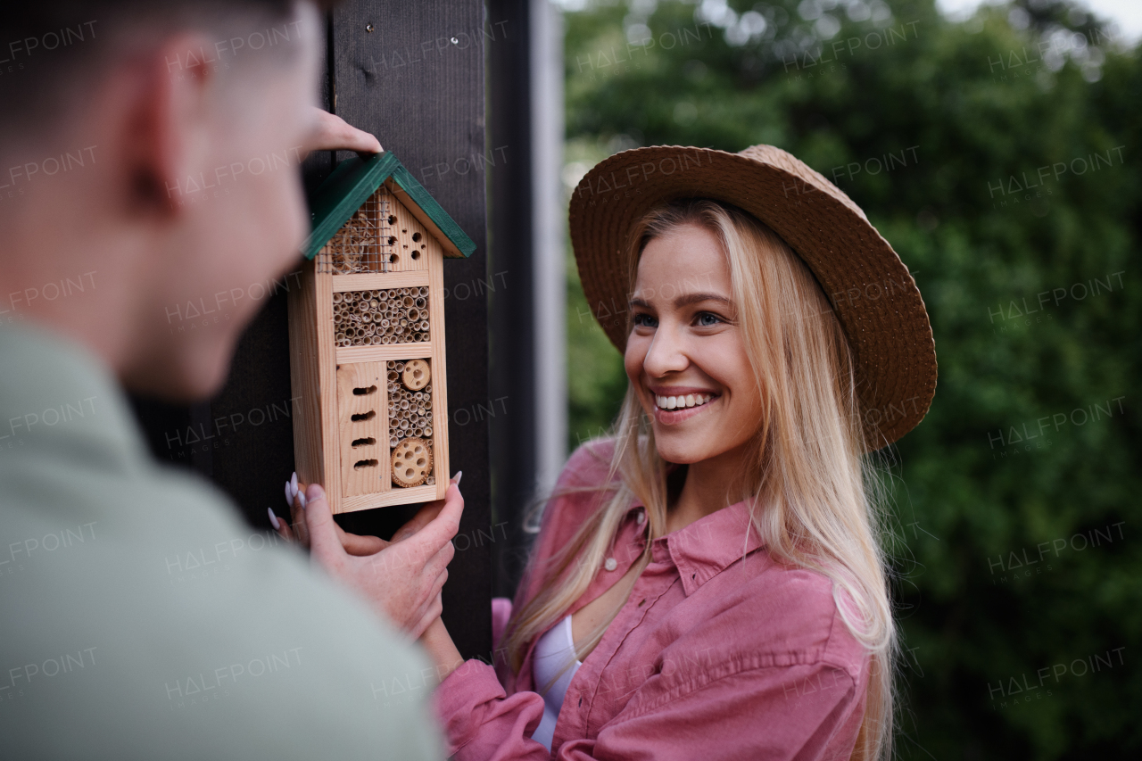 A young couple holding bug and insect hotel on terrace in garden, sustainable lifestyle.