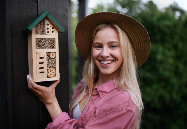 A young woman garedener holding bug and insect hotel on terrace in garden, sustainable lifestyle.