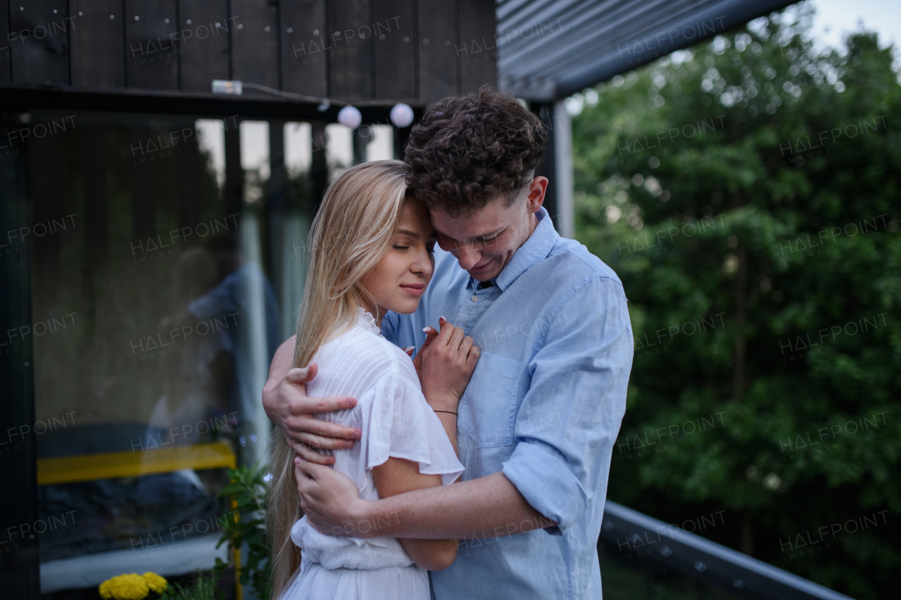 A young couple in love cuddling and kissing outdoors on terrace, weekend away in tiny house in countryside, sustainable living.