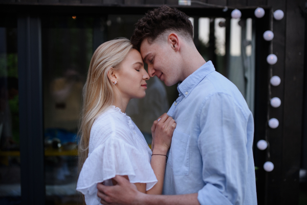 A young couple in love cuddling and kissing outdoors on terrace, weekend away in tiny house in countryside, sustainable living.