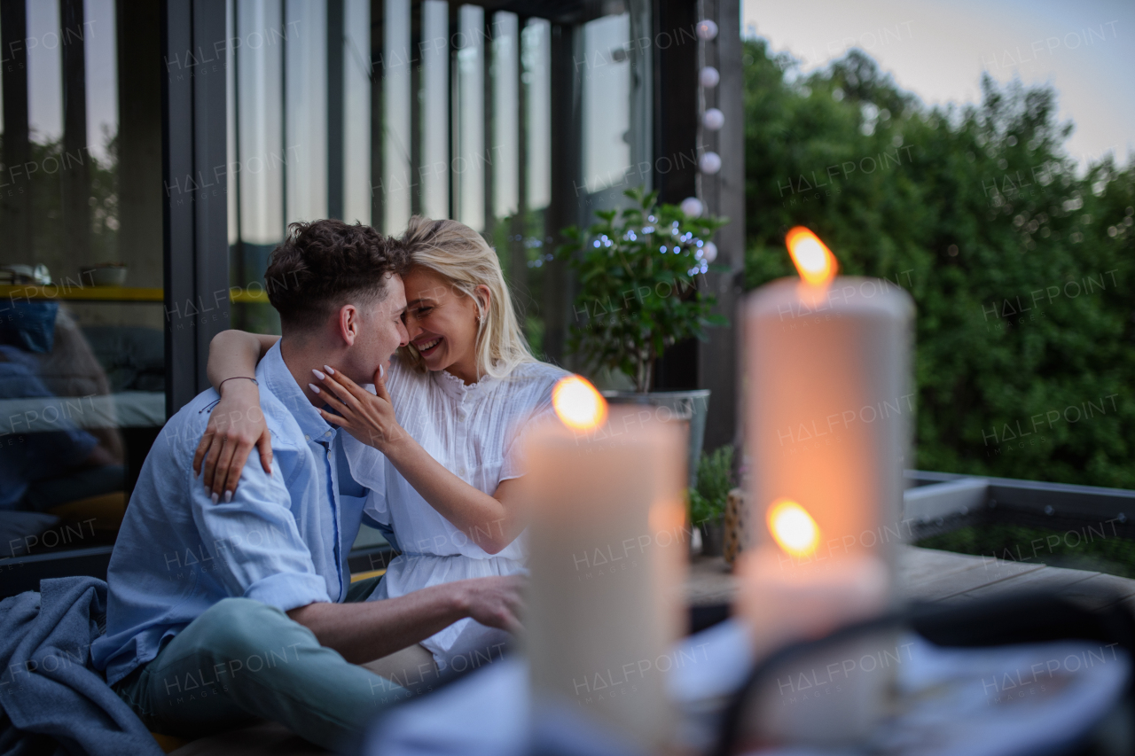 A young couple resting outdoors on terrace of tiny house in evening, weekend away in tiny house in countryside, sustainable living.