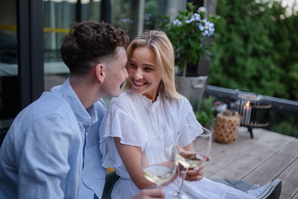 A young couple clinking with wine outdoors, weekend away in tiny house in countryside, sustainable living.