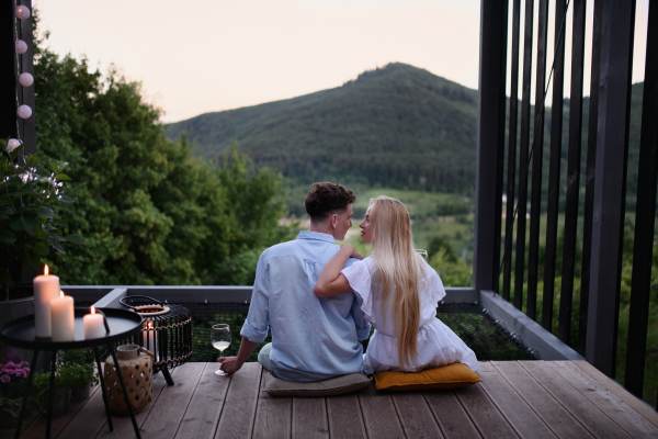 A young couple resting outdoors on terrace of tiny house in woods with view in evening, weekend away in tiny house in countryside, sustainable living.