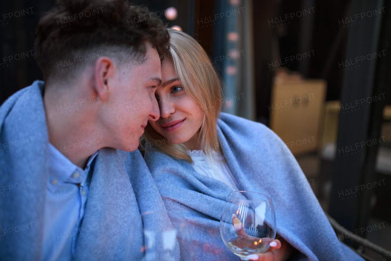 A young couple with wine resting outdoors on terrace in evening, weekend away in tiny house in countryside, sustainable living.