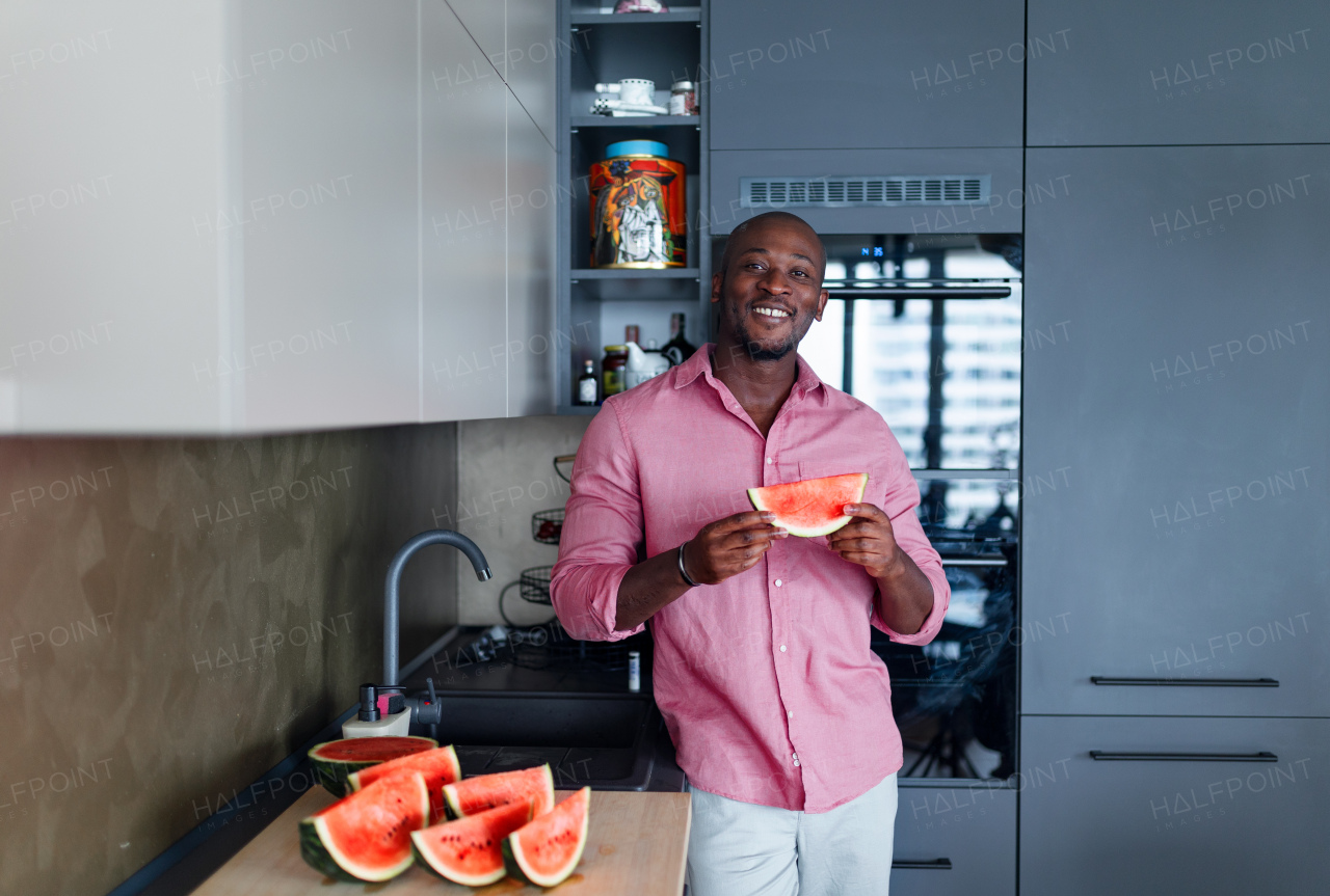 Multiracial man eating watermelon in his kitchen during hot summer.