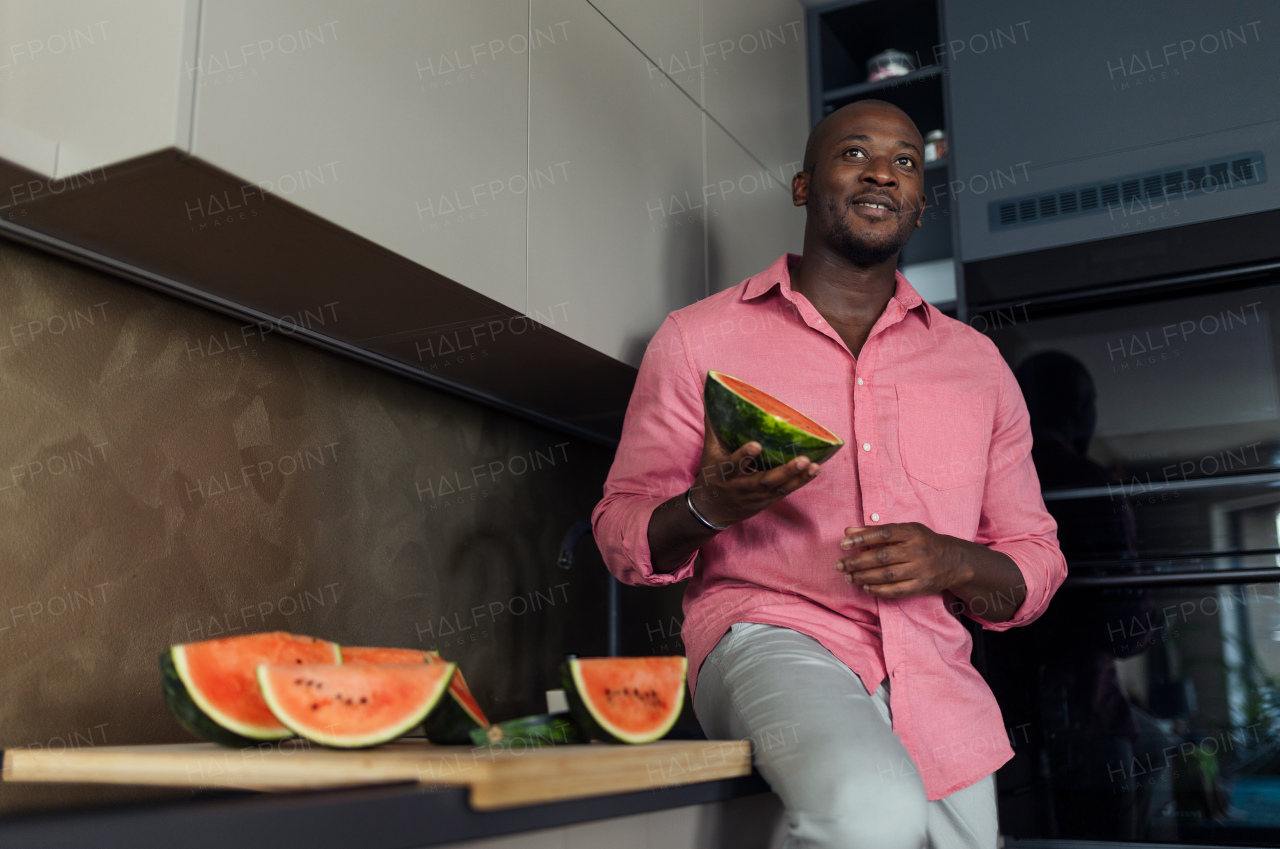 Multiracial man eating watermelon in his kitchen during hot summer.