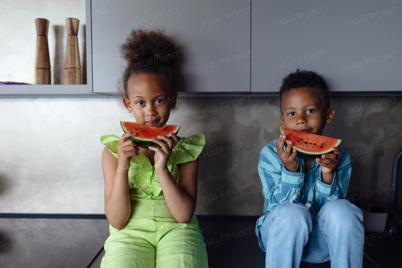 Multiracial kids eating a melon in kitchen during hot sunny days.