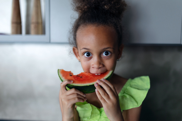 Multiracial girleating a melon in kitchen during hot sunny days.