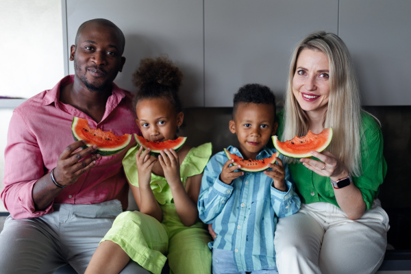 Multiracial family eating a melon in kitchen during hot sunny days.