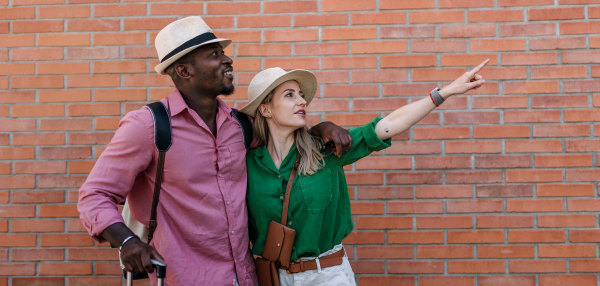 Young biracial couple travelling together with suitcases. Posing in front of brick wall.