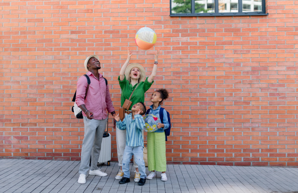 Multiracial family travelling together with small kids. Posing in front of a brick wall with beach ball.