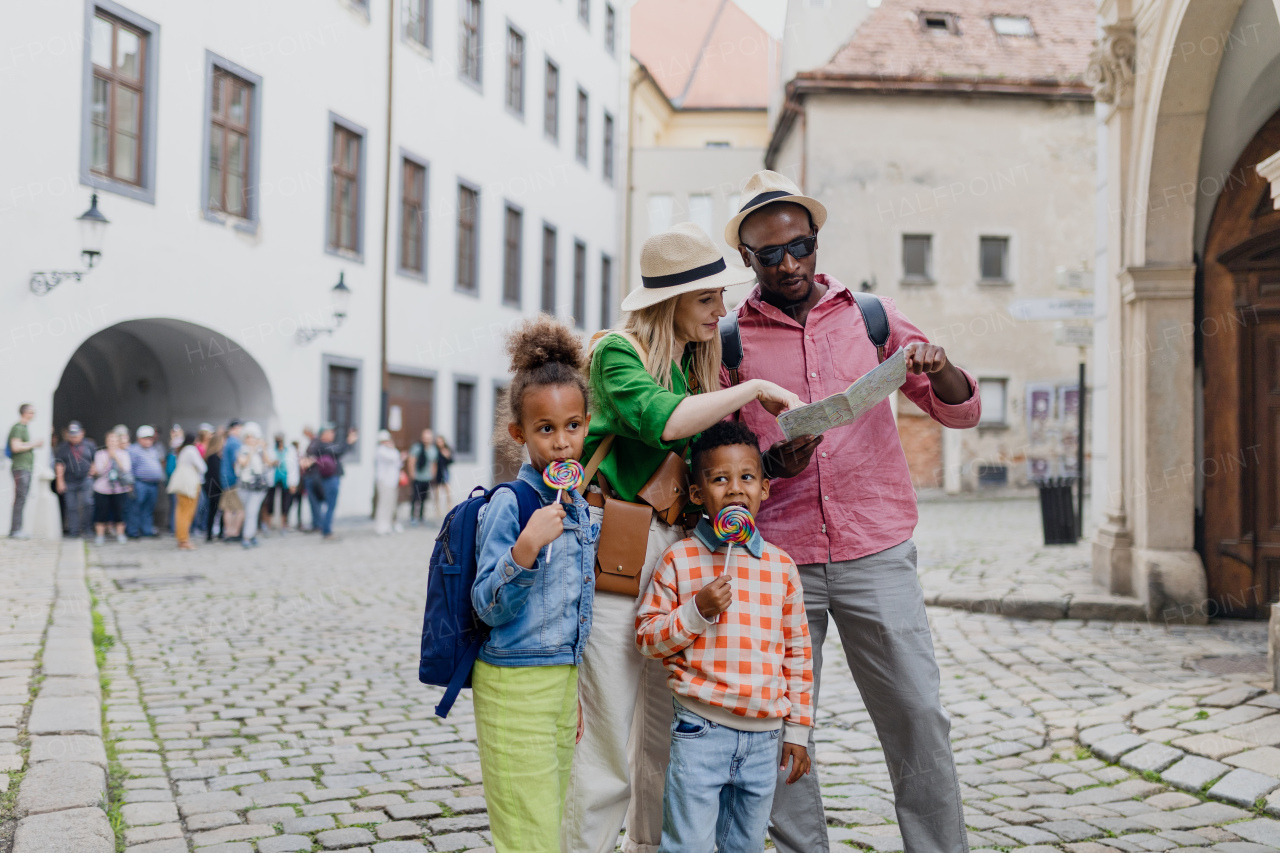 Happy multiracial family travel together with suitcases, walking in old city centre.