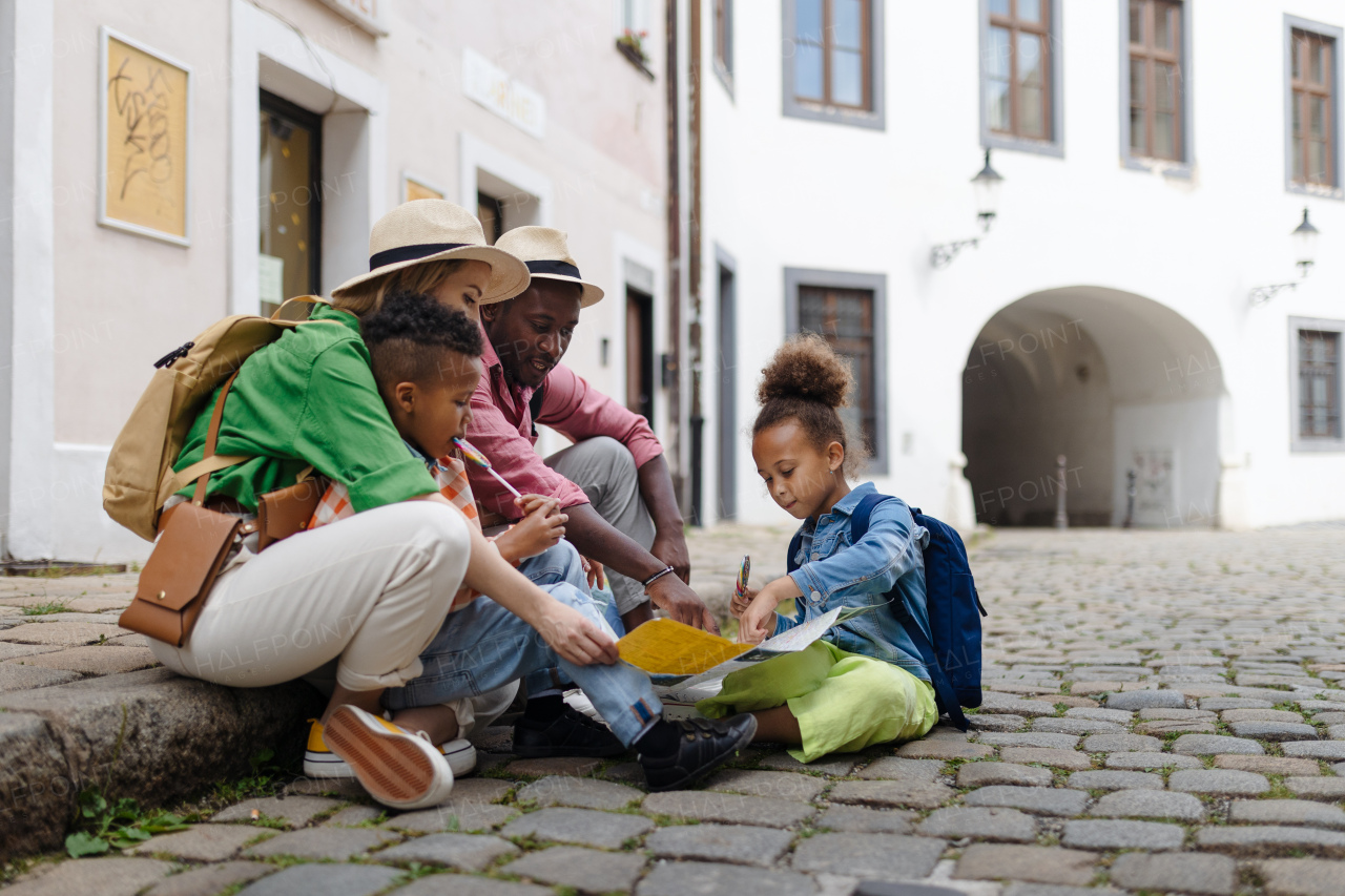 Multiracial family travel together in city centre, sitting on ground and looking at the paper map.