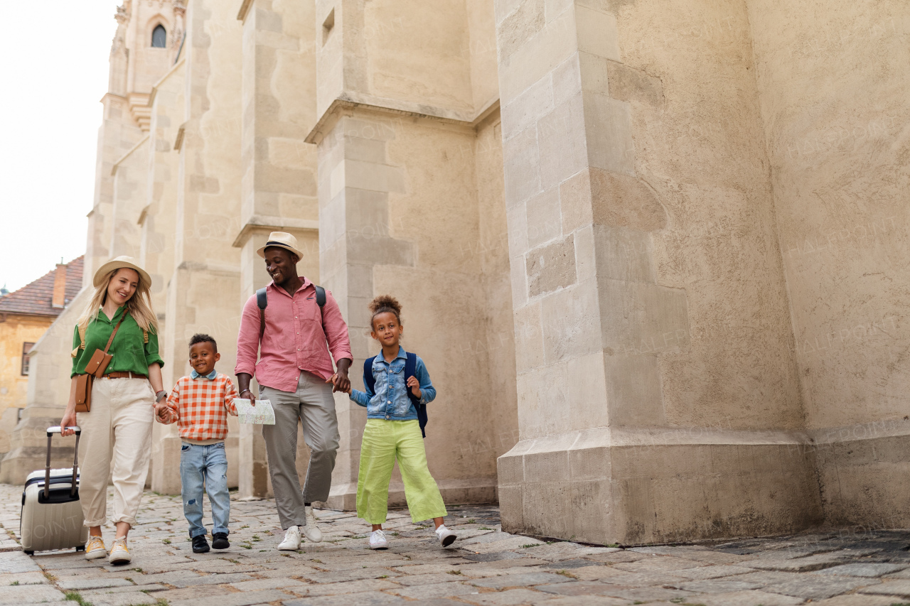 Happy multiracial family travel together with suitcases, walking in old city centre.