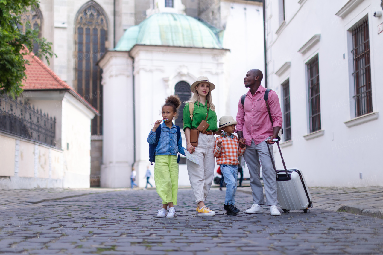 Happy multiracial family travel together with suitcases, walking in old city centre.