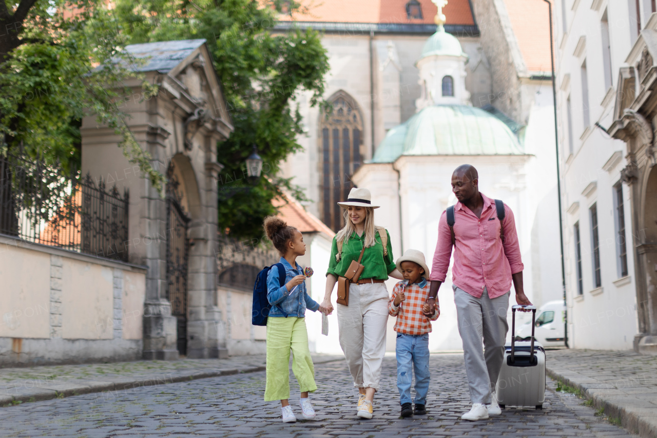 Happy multiracial family travel together with suitcases, walking in old city centre.