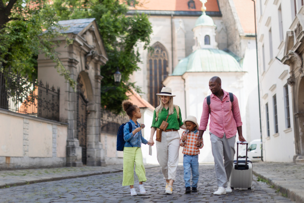 Happy multiracial family travel together with suitcases, walking in old city centre.