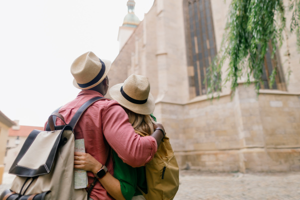 Multiracial family travel together in an old city centre, rear view.