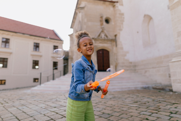 Multiracial girl playing outdoor with a bubble blower.