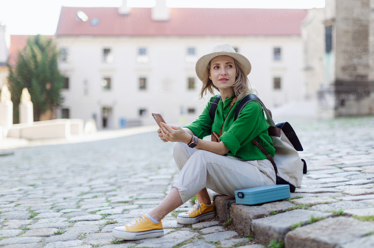 Young blond woman travel alone in old city centre, sitting and using smartphone.