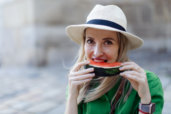 A young woman traveller eating watermelon in street during hot sunny day, summer vacation trip concept.