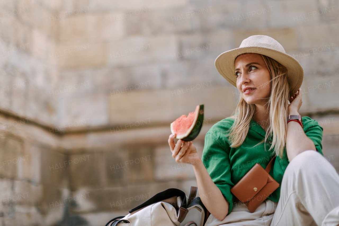 A young woman traveller eating watermelon in street during hot sunny day, summer vacation trip concept.