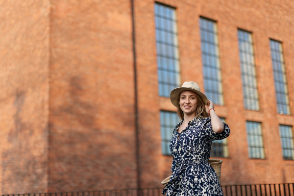 Young woman in a city during sunset, standing and posing in front of old brick building.