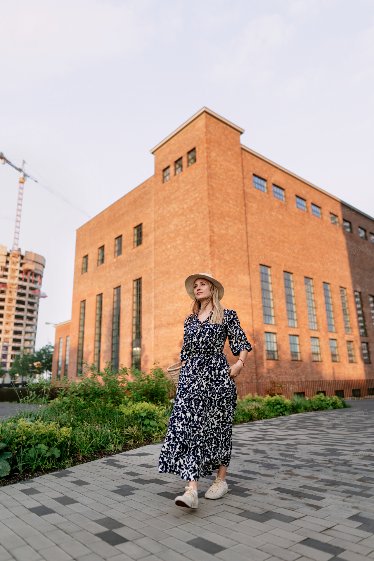 Young woman in a city during sunset, standing and posing in front of old brick building.